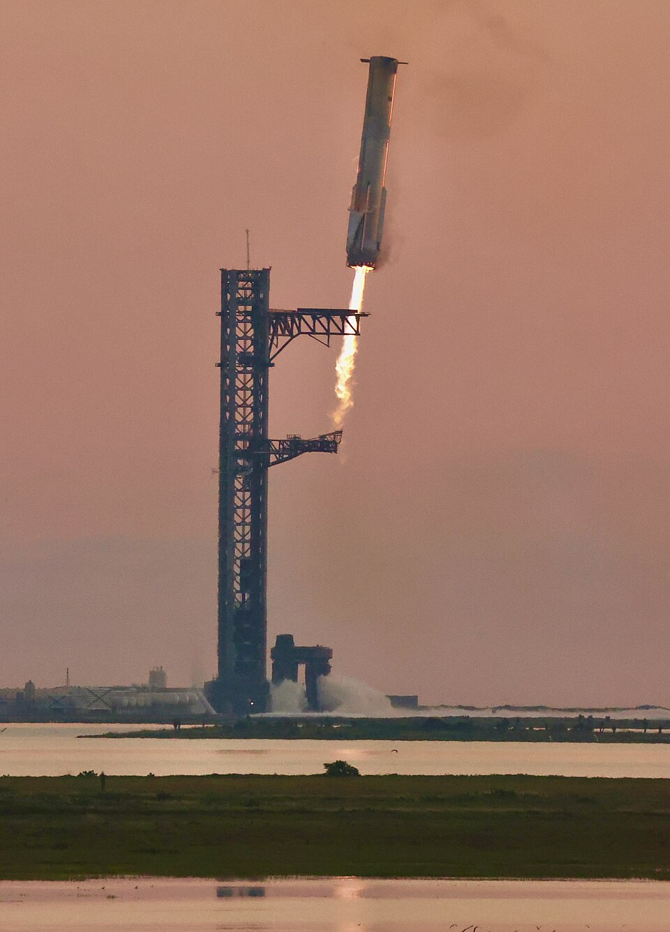 SpaceX Super Heavy booster descending toward the launch tower's catch arms, engines firing